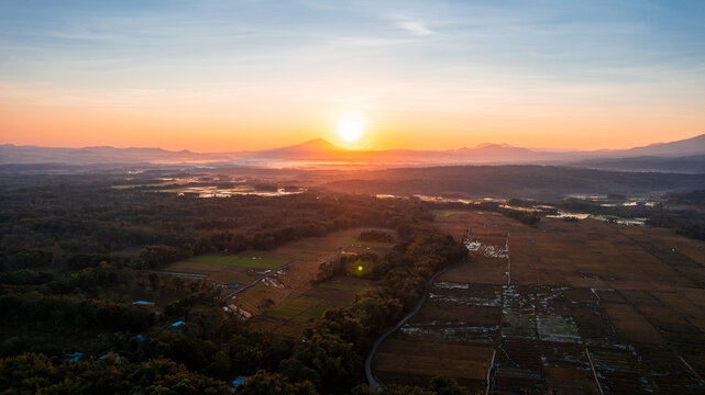 Aerial view of the lush landscape at sunrise with rolling hills, agricultural fields, and distant mountains in Bajawa, Nusa Tenggara Timur, Indonesia.