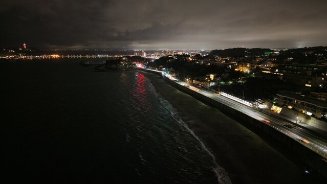 Aerial view of Shichirihama Beach at night, featuring the illuminated coastal road, dark ocean waves, and the glowing city lights of Kamakura, Kanagawa, Japan.
