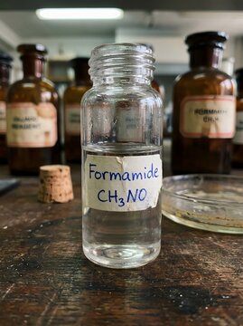 Glass specimen jar labeled Formamide CH3NO with handwritten chemical label among blurred vintage amber apothecary bottles on rustic lab table