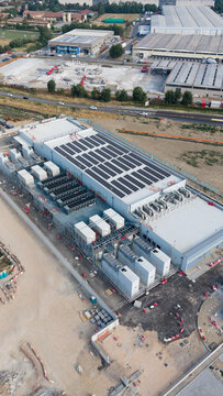Aerial view of the BYES MIL08 data center facility featuring a large roof with solar panels and cooling infrastructure, situated in an industrial area in Siziano, Lombardia, Italy.