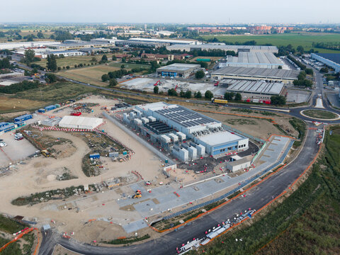 Aerial view of the BYES MIL08 data center construction site with industrial buildings, surrounding fields, and road infrastructure in Siziano, Lombardia, Italy.