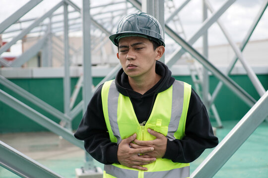 Male Construction Worker in Distress, Clutching His Stomach at Building Site