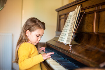 Young girl in yellow sweater playing piano with sheet music open. © Rawpixel.com