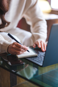Vertical closeup image of a woman writing on a notebook while working on laptop computer