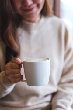 Vertical closeup image of a woman holding and drinking hot coffee in cafe