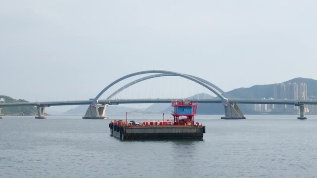 A large industrial barge boat on the water with Tseung Kwan O Cross Bay Bridge in the background, Hong Kong.