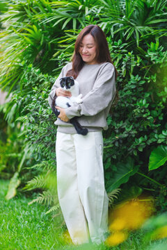 Vertical portrait of a woman holding a black and white colors cat in the garden