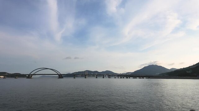 Timelapse of the iconic Tseung Kwan O Cross Bay Bridge with moving clouds and boats under a wide blue sky, Hong Kong.