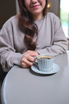 Vertical closeup image of a woman holding and drinking hot coffee in cafe
