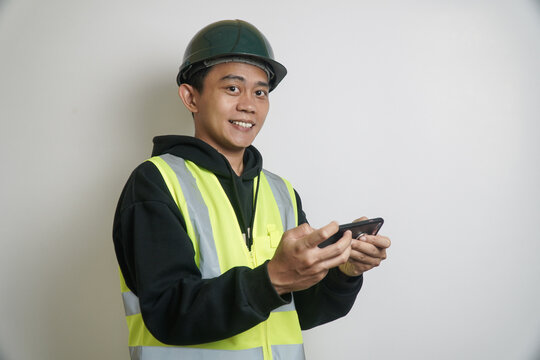 Smiling Worker in Hard Hat and Safety Vest Holding a Smartphone on White