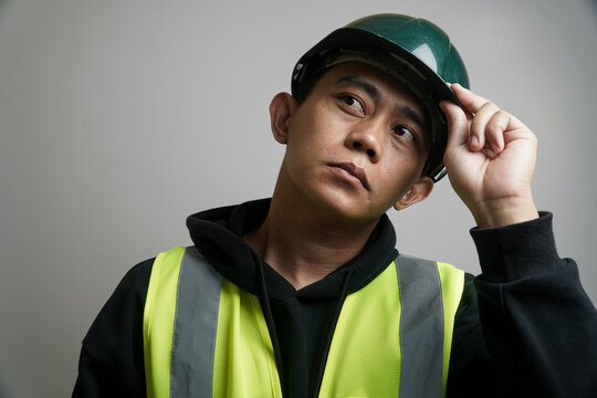 Thoughtful Young Man in Safety Vest and Hard Hat Looking Up During Work