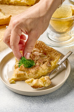 Hand placing peppermint garnish on golden rhubarb tart slice served on ceramic plate beside fork and teacup, with crumbly crust, glossy filling and warm soft natural light