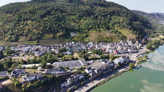 Aerial drone view of Bullay on the Moselle River in Rhineland-Palatinate, Germany, surrounded by vineyards and forested hills. Scenic Moselle Valley landscape with reflections of clouds in the calm ri