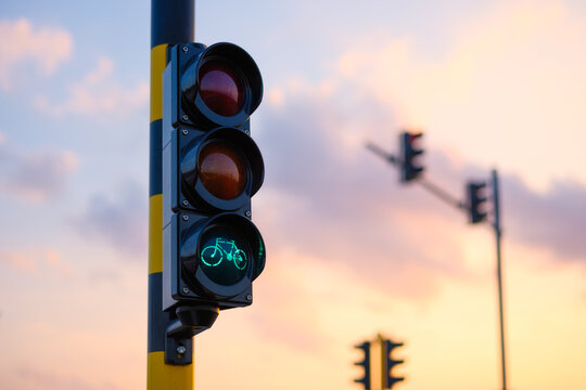 Green bicycle traffic light glowing against a sunset sky. Traffic signal for cyclists on an urban street at dusk.