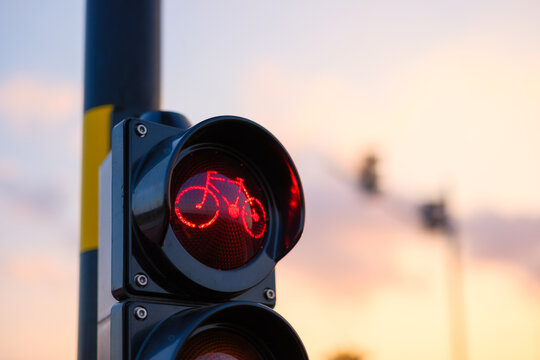 Red bicycle traffic light glowing against a sunset sky. Traffic signal for cyclists on an urban street at dusk.