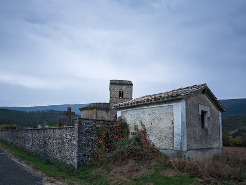 Romanesque church and stone walled cemetery with crosses under a cloudy sky