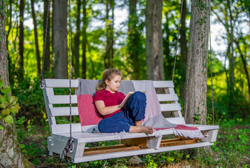 Fototapeta premium Child playing and dreaming on swing outside. Happy child enjoying playful activity in garden. Young kid sitting calmly on swing in nature. Child enjoying freedom and fun on backyard swing.