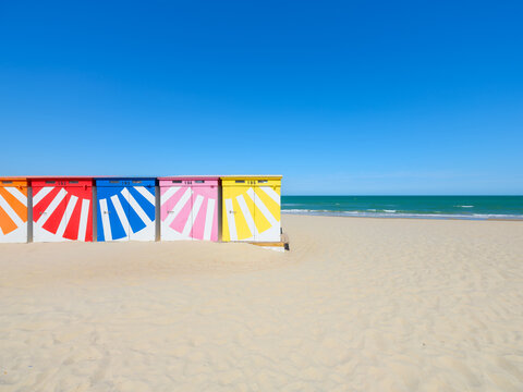 Colorful beach huts on a sandy shore by the sea under a clear blue sky. Summer vacation and travel landscape.