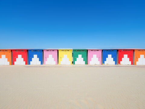 Colorful beach huts on a sandy shore by the sea under a clear blue sky. Summer vacation and travel landscape.