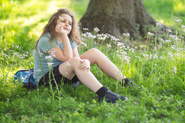 Naklejka premium Child portrait shows summer innocence. Relaxed child sits in green meadow. Smiling child enjoys sunny nature. Child lifestyle feels peaceful and authentic.