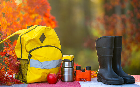 Hiking backpack with travel equipment. Hiking gear beside thermos. Outdoor hiking bag in daylight. Autumn hiking setup near foliage. Camping equipment with yellow backpack.