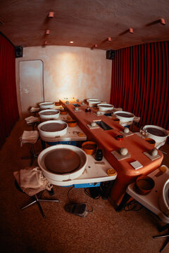 Empty ceramics studio prepared for a hands-on masterclass, with multiple pottery wheels, clay balls, tools, water bowls, sponges, towels and stools, shot on wide-angle fisheye lens