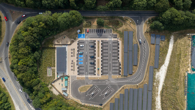 Aerial view of a modern parking lot featuring solar panel arrays, marked parking spaces, and surrounding lush green trees in Winchester, England, United Kingdom.