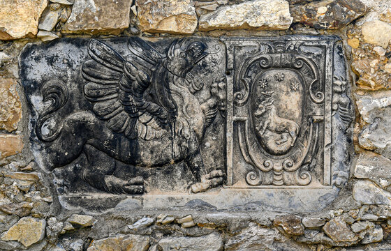Ancient stone reliefs depicting a heraldic griffin and a noble coat of arms on a wall at Castello Brown in Portofino, Italy