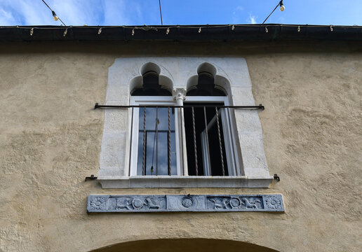 Historic medieval mullioned bifora window with a carved stone relief on a rustic wall at Castello Brown in Portofino, Italy