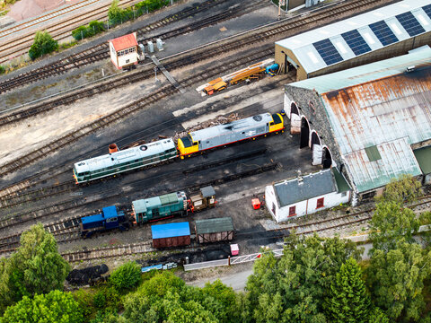 Aerial view of the Strathspey Railway depot with diesel locomotives parked on tracks near the historic engine shed and workshop buildings in Aviemore, Scotland, United Kingdom.