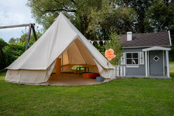 Canvas glamping tent beside a wooden children’s playhouse in a green summer garden © Edijs