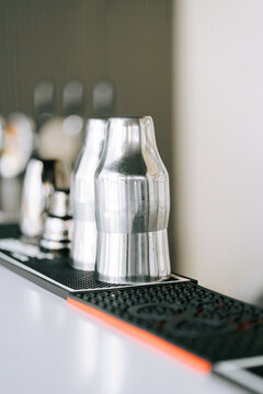 Metal cocktail shaker resting on a black rubber bar mat inside a bright modern cafe during the day