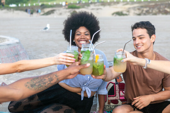 Group of friends enjoying drinks on the beach, smiling and toasting.