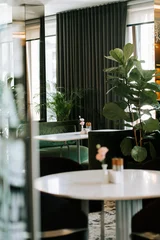 Fotobehang Horeca Modern cafe interior with lush green plants and round tables during a bright afternoon in the city  © Darius