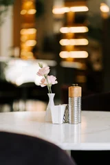 Fotobehang Horeca Pink flowers in a small vase on a marble restaurant table during a quiet afternoon in the evening  © Darius