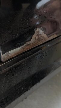 Close-up of a hand using sandpaper to remove rust from a car door trim, showing the gradual cleaning process with visible dirt and moisture on the surface
