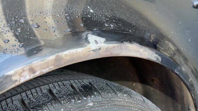Close-up of a hand using sandpaper to remove rust from a car door trim, showing the gradual cleaning process with visible dirt and moisture on the surface