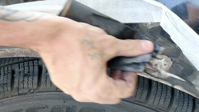 Close-up of a hand using sandpaper to remove rust from a car door trim, showing the gradual cleaning process with visible dirt and moisture on the surface