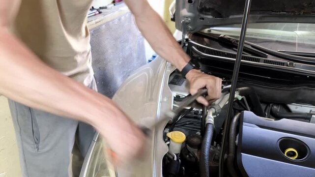 Male mechanic using a ratchet wrench to tighten bolts on a car engine in a garage, showcasing detailed work on automotive components and tools