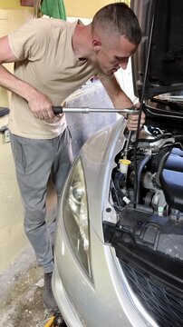 Male mechanic using a ratchet wrench to tighten bolts on a car engine in a garage, showcasing detailed work on automotive components and tools