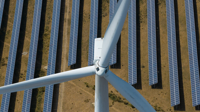 Aerial view of a wind turbine standing in front of extensive rows of solar panels at the Chelveston Renewable Energy site in Chelveston, England, United Kingdom.