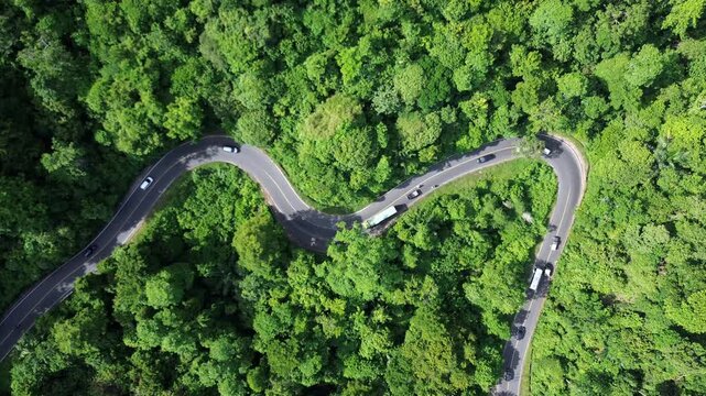 Cinematic aerial view of a winding mountain road where a small vehicle attempts to overtake a large vehicle ahead of it.