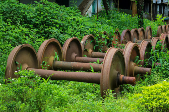 Old Rusty Train Axles and Wheels Stored Outdoor Overgrown with Green Grass