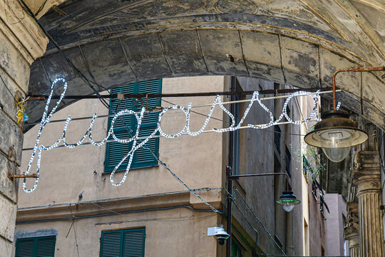 Illuminated text sign fugassa (focaccia in dialect) under historic stone arches in the old town of Genoa, Liguria, Italy