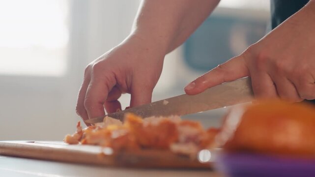 Close-up of hands pulling apart cooked meat on wooden board beside bun in sunlit kitchen, with knife steadying food and visible finger movement during homemade meal preparation, with hand, shredding