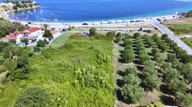 Aerial view of Toroni in Sithonia, Halkidiki, Greece, showing a busy Mediterranean beach with turquoise crystal-clear water, swimmers, sunbeds and beachfront hotels on a sunny summer day.