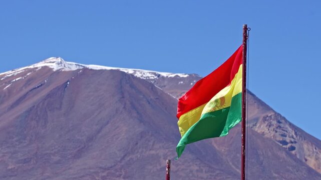 National flag of bolivia waving proudly in the wind with a beautiful snow capped mountain in the background under a clear blue sky. Uyuni salt flats, bolivia