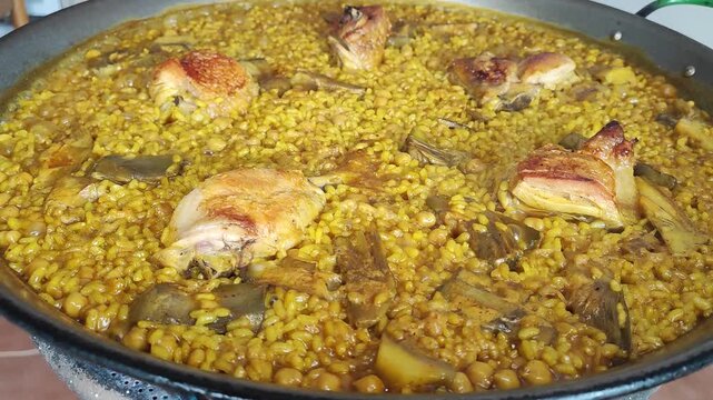 Arroz con pollo, alcachofas y garbanzos. Una paella con trozos de carne dorados. 