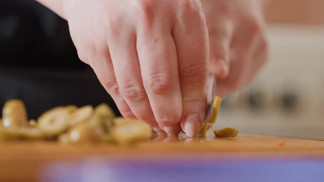 Close-up kitchen scene showing hands gathering, pressing, and moving chopped garlic on wooden board, with warm light, rough texture, scattered pieces, and active food prep, with garlic, hand, kitchen