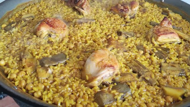   Arroz con pollo, alcachofas y garbanzos. Una paella con trozos de carne dorados.